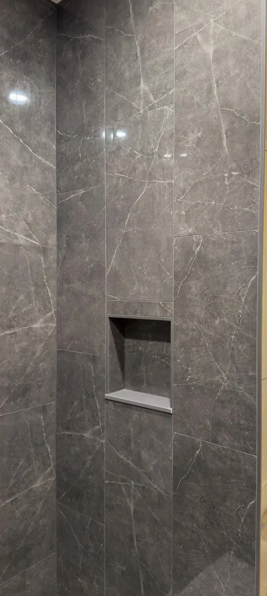 Large-format marble-look shower walls with a recessed niche