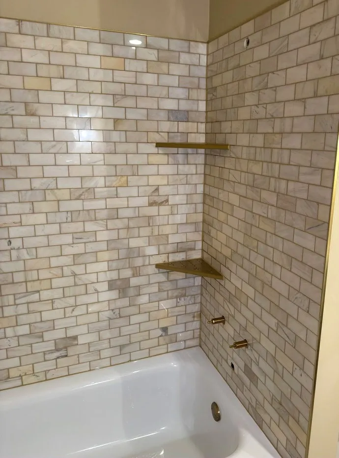 Tub surround in marble subway tile with brass shelves and fixtures
