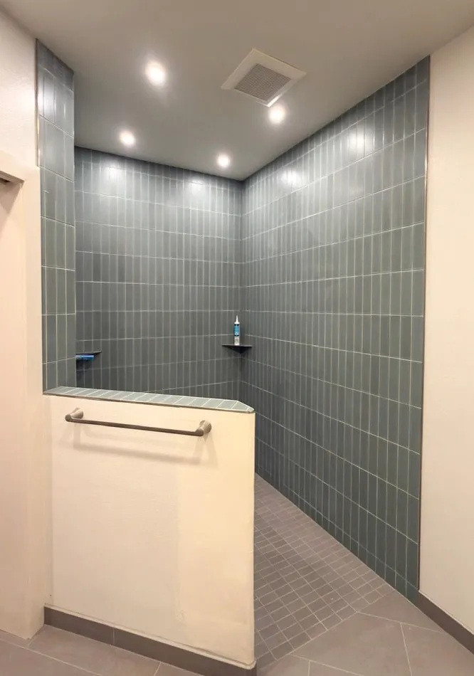 Walk-in shower with vertical stacked teal tile and corner shelves
