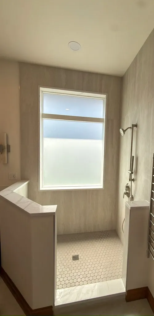 Walk-in shower with marble-look walls, a frosted window and a penny tile floor