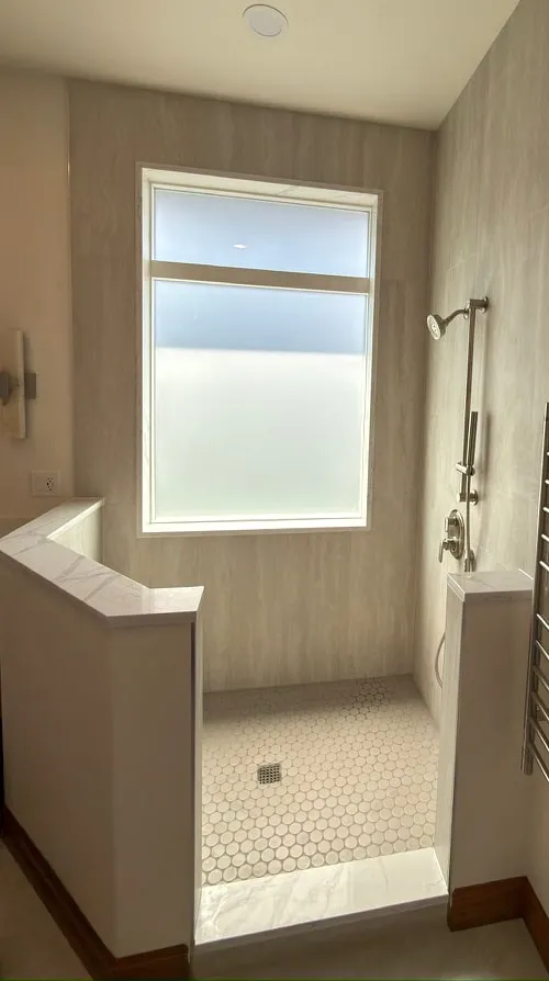 Walk-in shower with marble-look walls, a frosted window and a penny tile floor